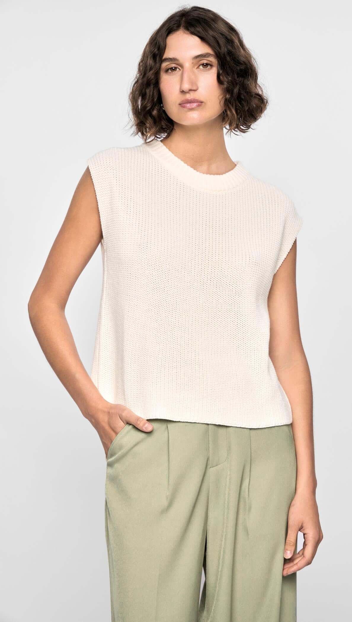 Model wearing the Quincey Knit Tank, a soft neutral sleeveless top with a boxy fit and wide ribbed armholes, paired with tailored pants.