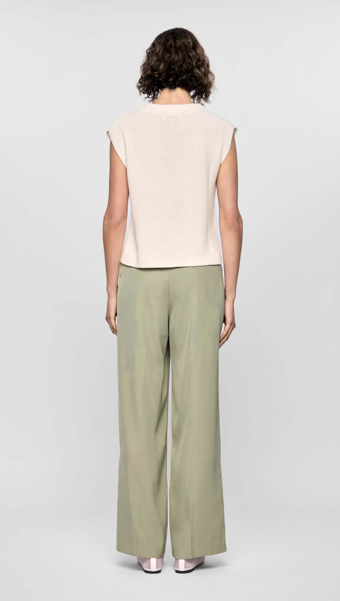 Model wearing neutral beige top and relaxed wide-leg green pants from behind, showcasing a modern, comfortable style.