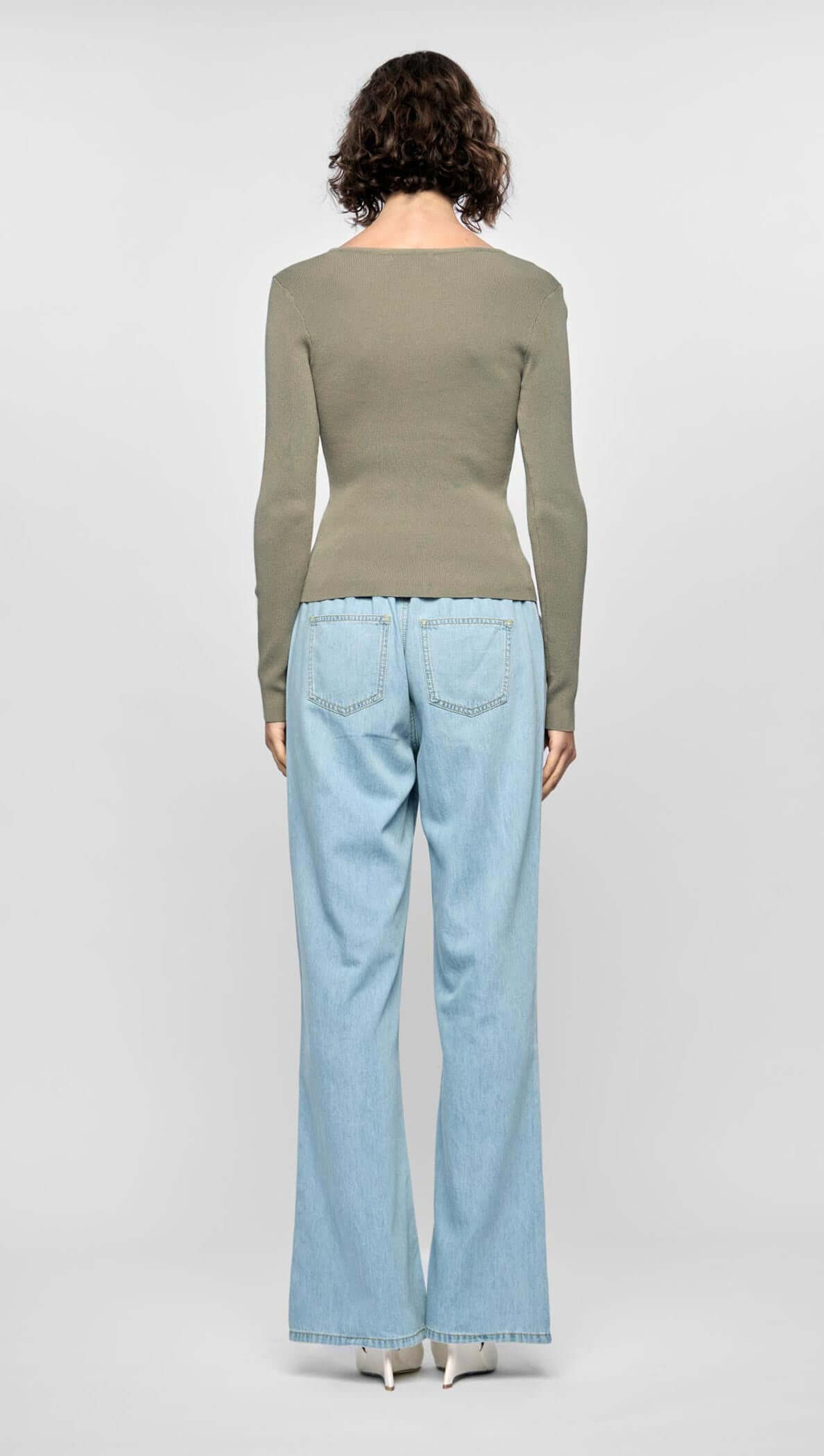 Model wearing the Mira Twist Knit Top in khaki with flared denim jeans from the back, showcasing a fitted silhouette.