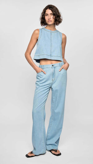 Model wearing the Amelia Chambray Top with raw-edge detailing in light chambray blue, paired with matching denim pants.