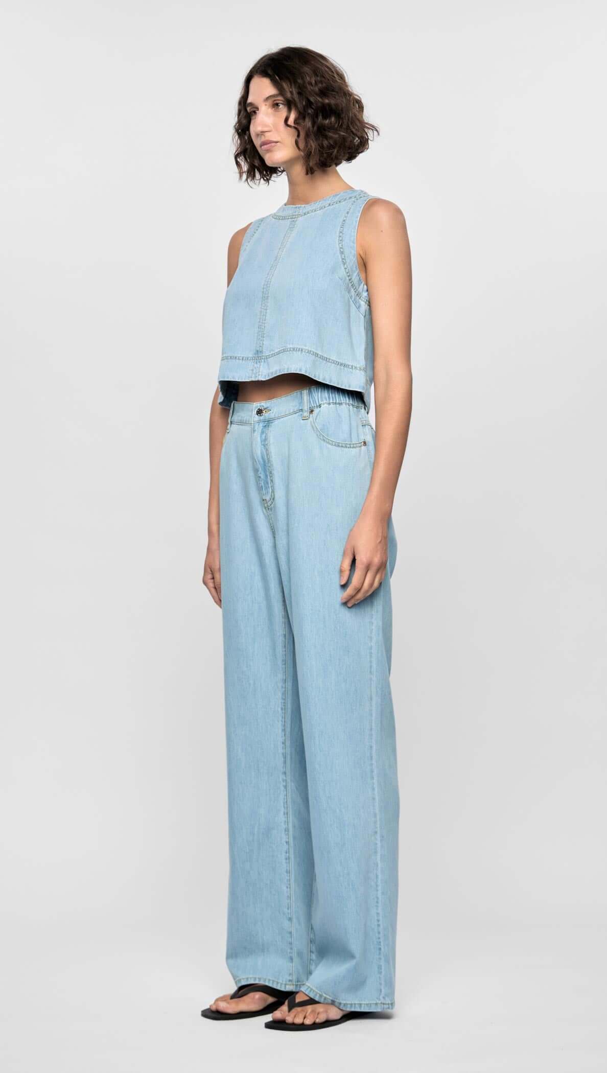 Model wearing Amelia Chambray Top, a cropped sleeveless top in light chambray blue, paired with matching wide-leg jeans.