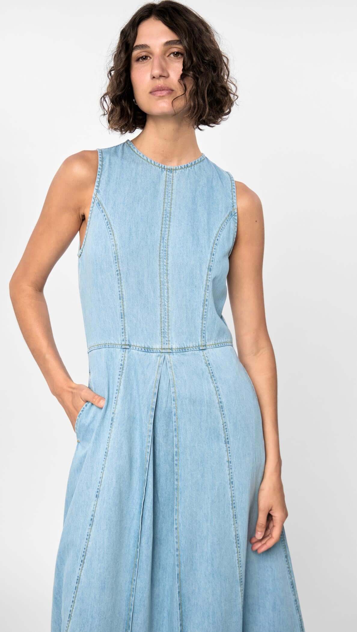 Model wearing the Amelia Chambray Midi Dress in light blue, showcasing sleeveless design, panelled fit, and side pockets.