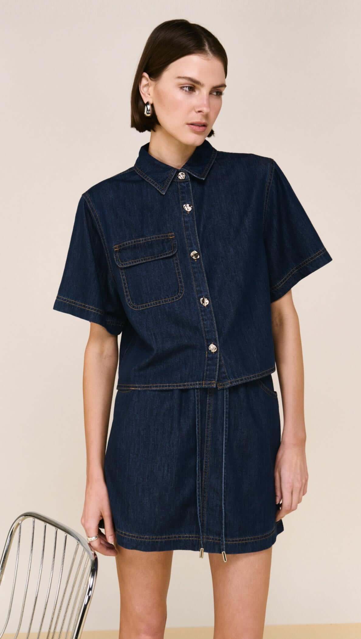 Denim Cropped Short-Sleeve Shirt featuring a structured cropped design and tailored lines, styled with a skirt.