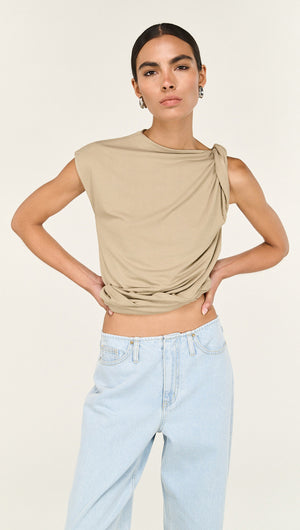 Model wearing a beige draped top with knotted shoulder detail paired with light wash straight leg denim jeans.