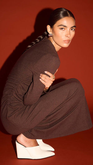 Gather Detail Long Sleeve Midi Dress in Chocolate modeled by a woman in a stylish crouch on a red background.