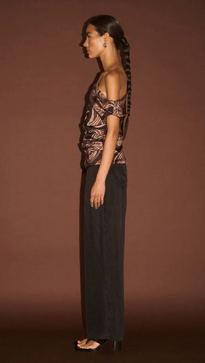 Side view of a model wearing an Abstract Leaf Print One Shoulder Top paired with black pants, showcasing a stylish modern outfit.