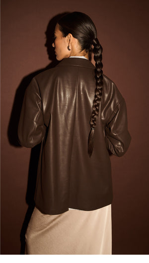 Model wearing a Chocolate Relaxed Vegan Leather Blazer, showcasing the back view against a dark background.