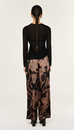 Back view of a woman wearing Abstract Leaf Print Relaxed Silky Pants paired with a black long-sleeve top.