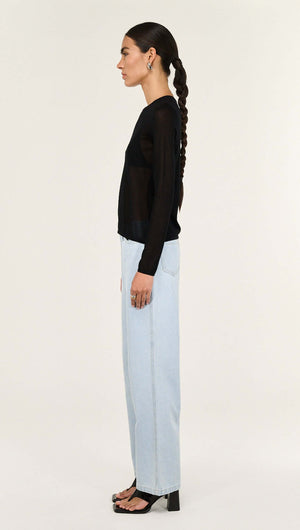 Model showcasing the Black Ruched Detail Sheer Knit Top styled with light blue jeans, emphasizing a contemporary fashion look.