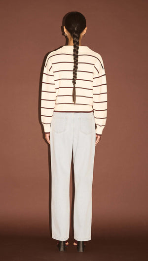 Back view of a model wearing a Chocolate Stripe Polo Knit Jumper with light blue jeans against a brown background.