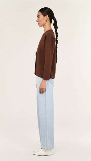 Chocolate Sculptured Soft Cardigan with Hardware Detail modeled by a woman in profile wearing light blue pants.