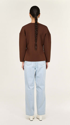 Back view of a model wearing the Chocolate Sculptured Soft Cardigan with Hardware Detail paired with light blue jeans.