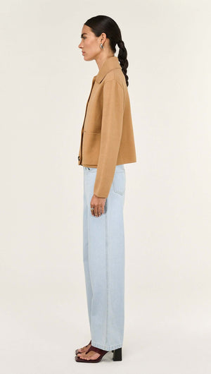 Side view of model wearing a Caramel Knitted Barn Jacket with light blue jeans.