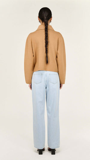 Back view of a model wearing a Caramel Knitted Barn Jacket paired with light blue jeans.