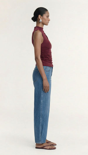 Model showcasing Burgundy High Neck Ruched Jersey Top paired with blue jeans from a side view.