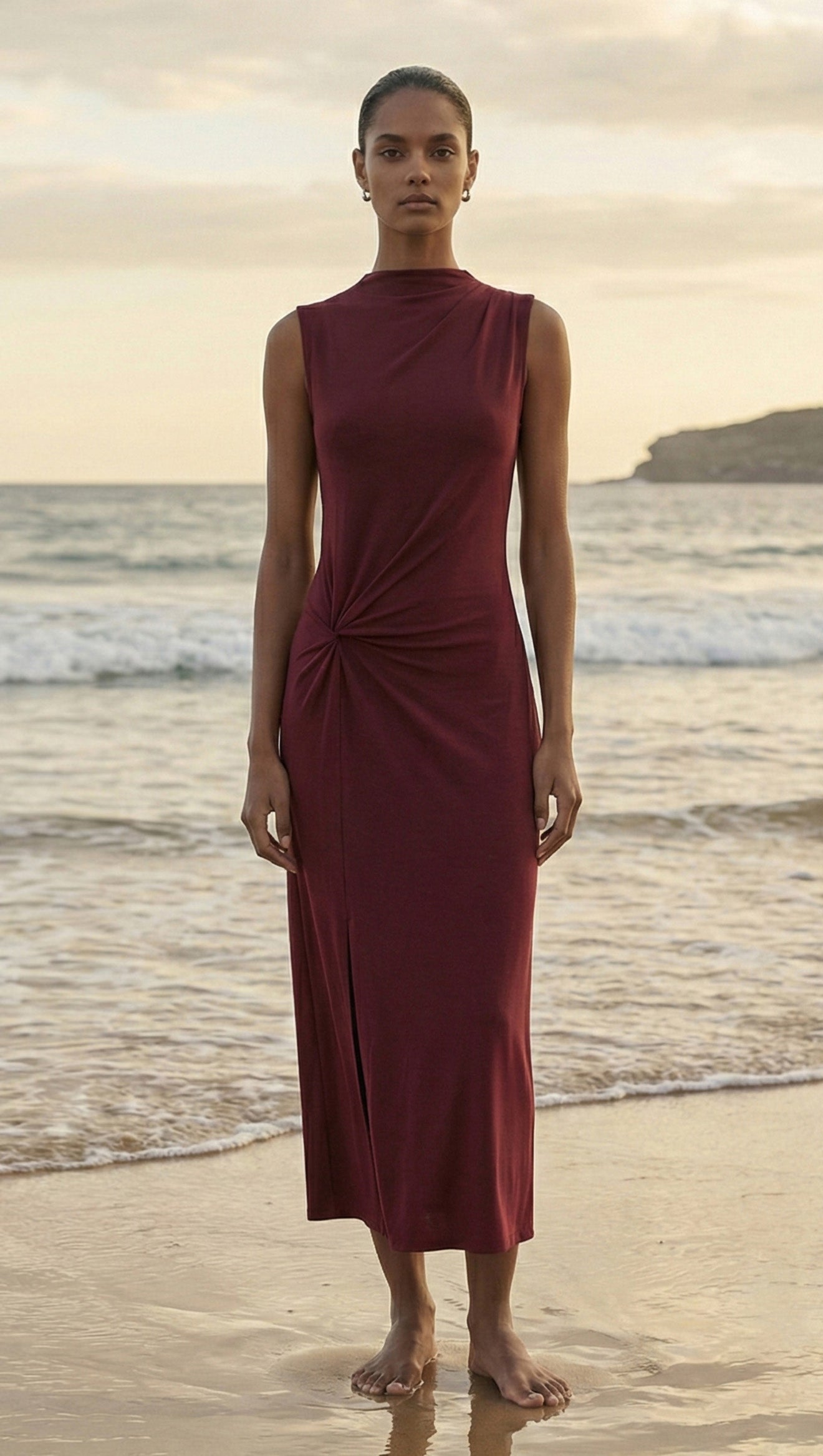 Burgundy Twist Detail Jersey Midi Dress worn by a model standing on the beach with ocean in the background.