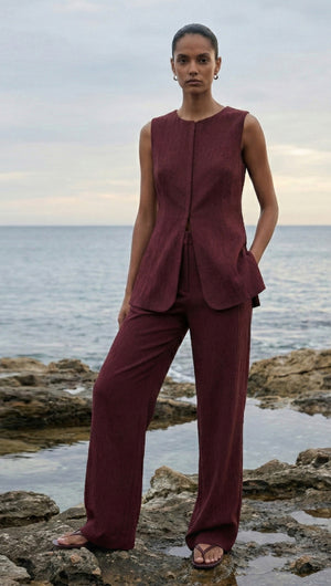 Model wearing a burgundy round neck textured vest with matching pants by the sea.