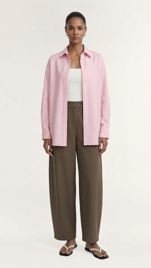 Model wearing a pink striped shirt and khaki structured barrel leg pant, showcasing modern relaxed tailoring in a minimalistic style.
