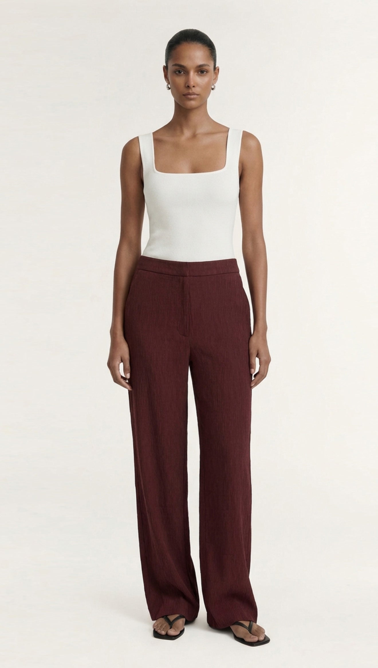 Model wearing Textured Burgundy Relaxed Fit Pant with a white tank top, showcasing stylish relaxed tailoring.