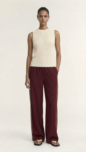 Woman wearing a cream sleeveless top and Burgundy Pinstripe Relaxed Pant, standing against a light backdrop.