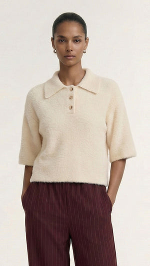 Model wearing a Fluffy Knit Polo Top in Cream with a collared neckline and short sleeves, paired with dark striped trousers.