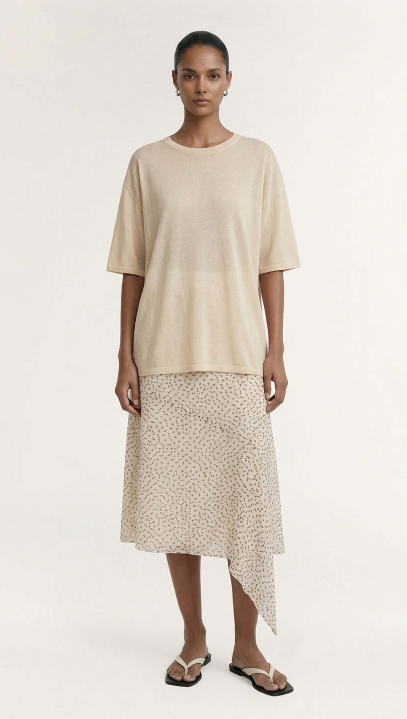 Model wearing a White Round Neck Oversized Knit Tee with brown pants, seated on a chair.