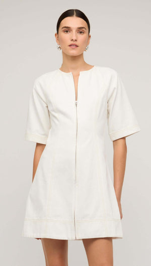 Model showcasing a white denim mini dress with a front zip and short sleeves on a neutral background.