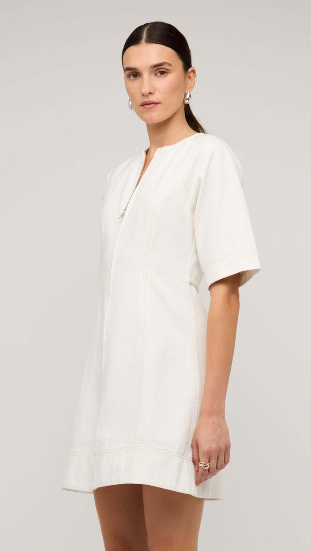 Model wearing a stylish white denim mini dress with a front zip, featuring short sleeves and a relaxed fit.