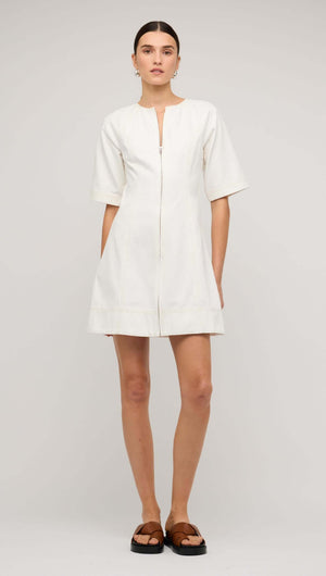 White denim mini dress with front zip, featuring short sleeves and a flared skirt, modeled by a woman.