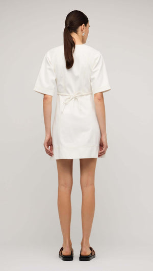 Back view of a woman wearing a white denim mini dress with short sleeves and belt detail.