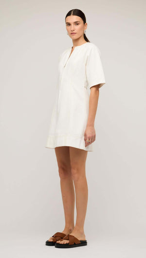 Model wearing a white denim mini dress with front zip, showcasing a relaxed fit and short sleeves.
