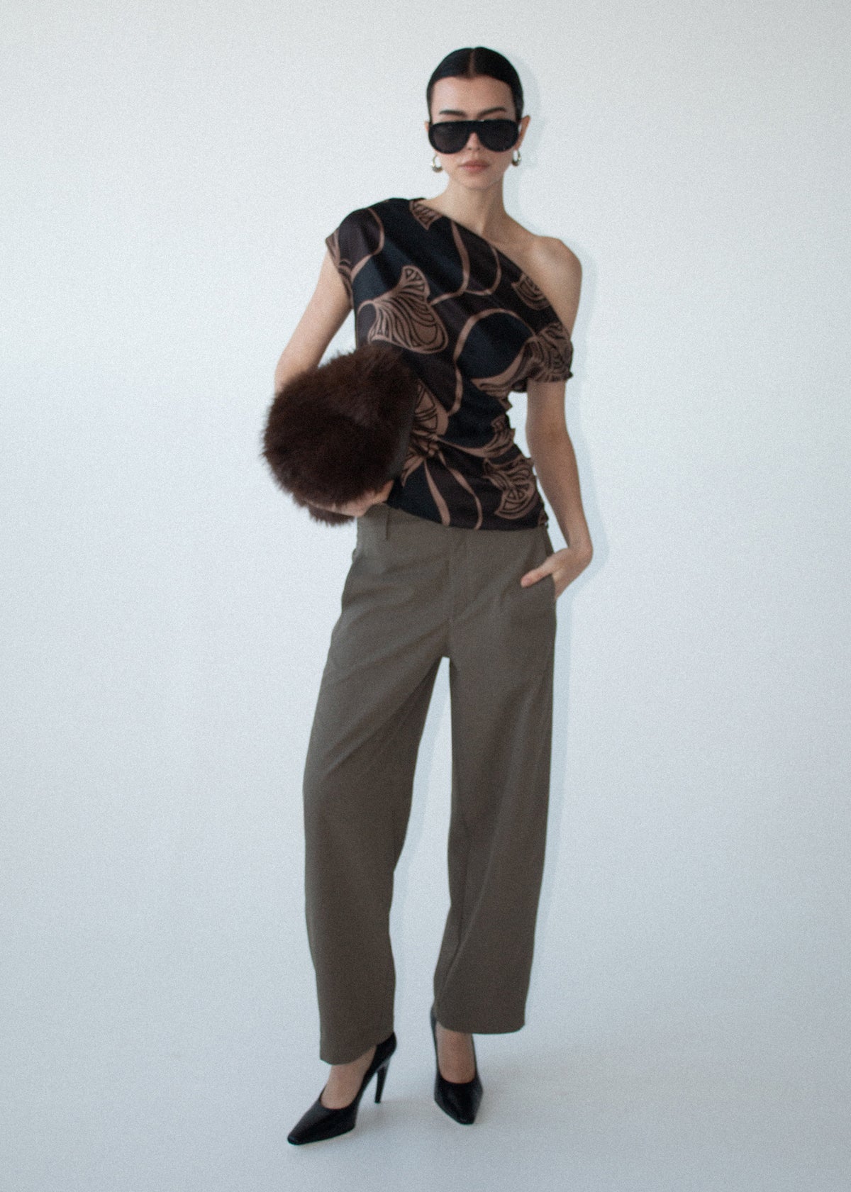 Model wearing Abstract Leaf Print One Shoulder Top with abstract leaf print in chocolate tones and a fluid drape, turned to the side.