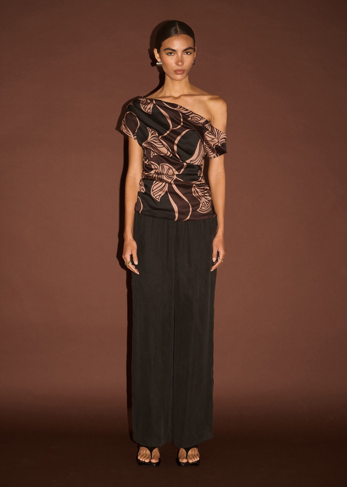 Model wearing Abstract Leaf Print One Shoulder Top, showing abstract leaf print in chocolate tones and a fluid drape.