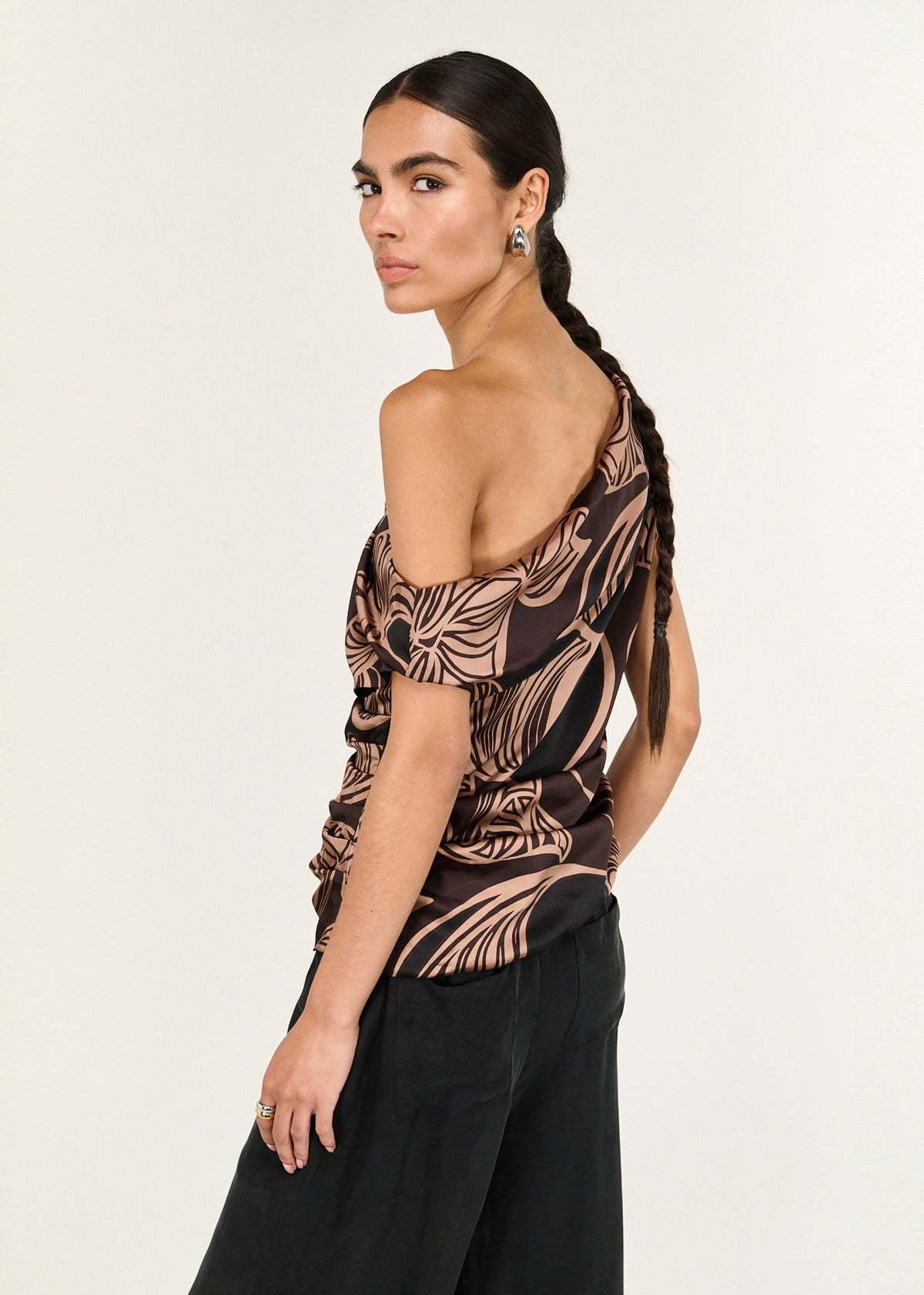 Angled view of the Abstract Leaf Print One Shoulder Top with abstract leaf print in chocolate tones and a fluid drape.