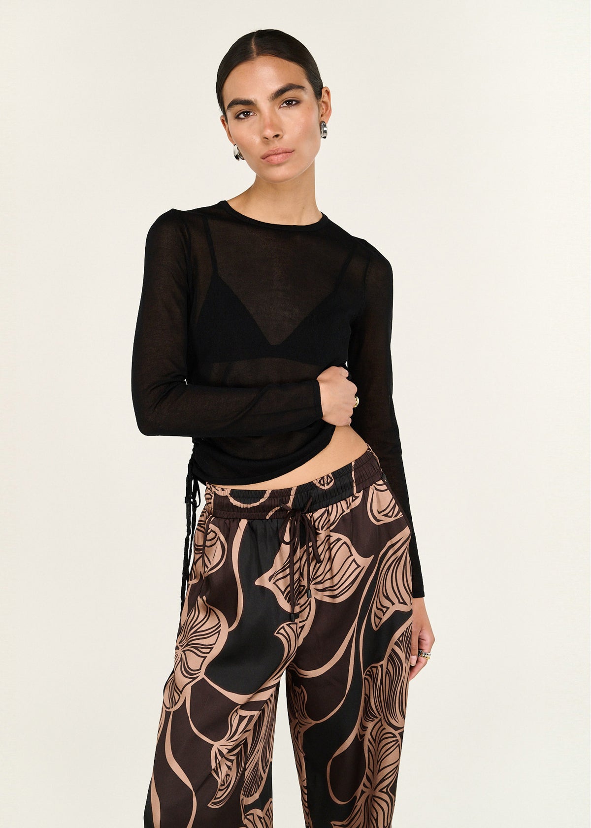 Model wearing Abstract Leaf Print Relaxed Silky Pants with abstract leaf print in chocolate tones and a soft drape, turned to the side.