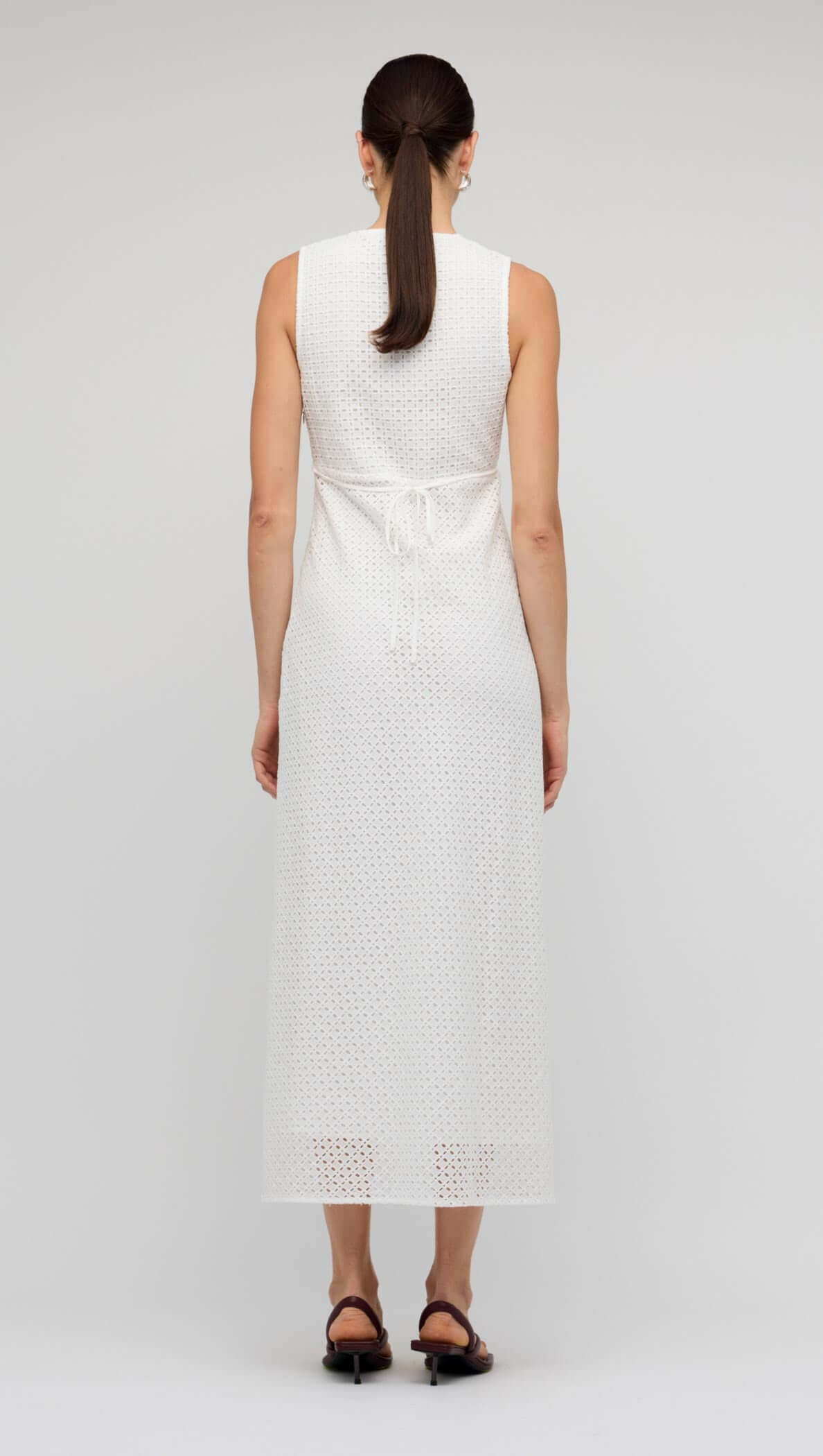 Back view of White Broderie Bias Midi Dress showcasing the sleeveless design and adjustable waist tie for a flattering fit.