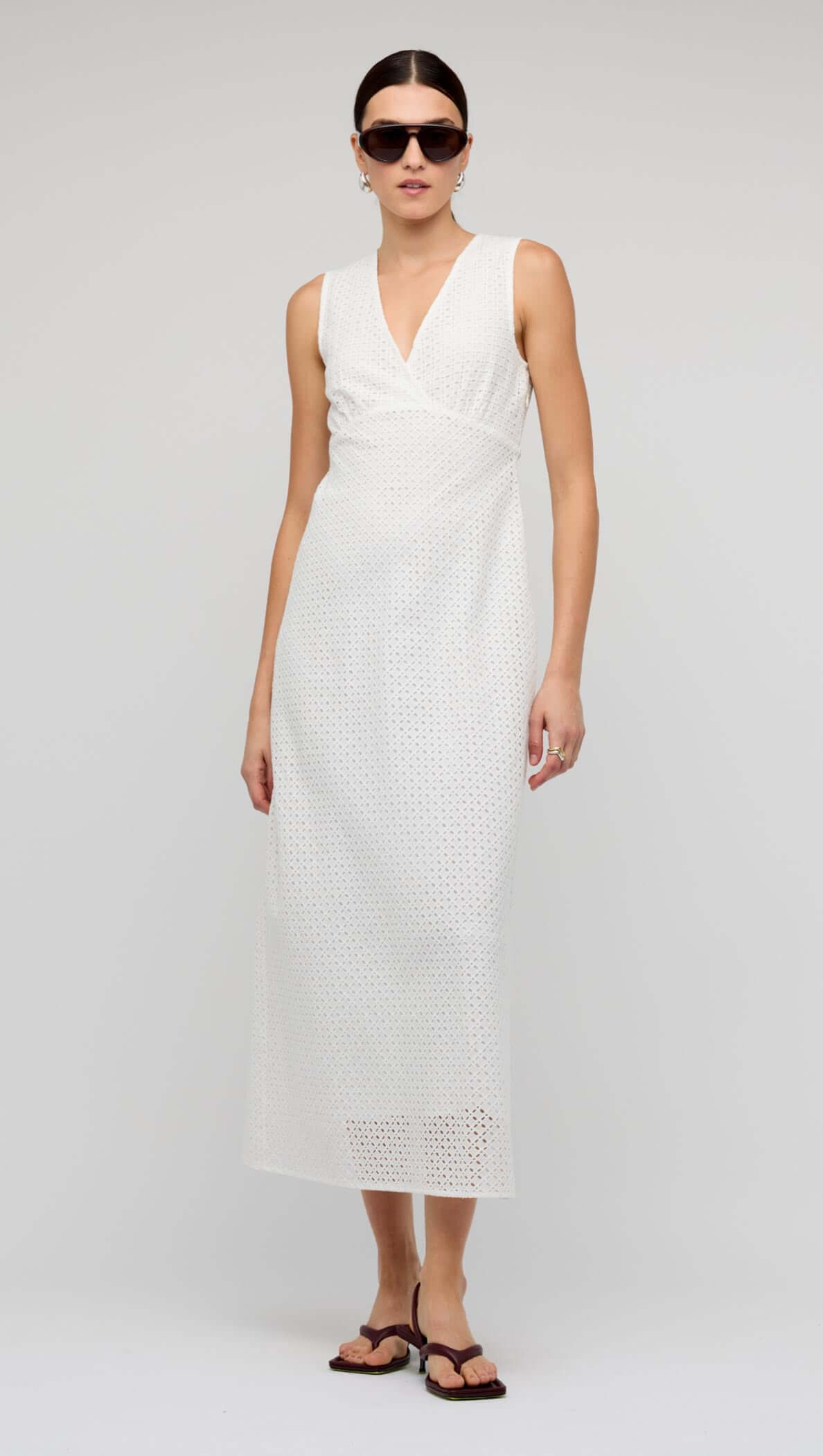 Model wearing the White Broderie Bias Midi Dress featuring a V-neck and sleeveless design.