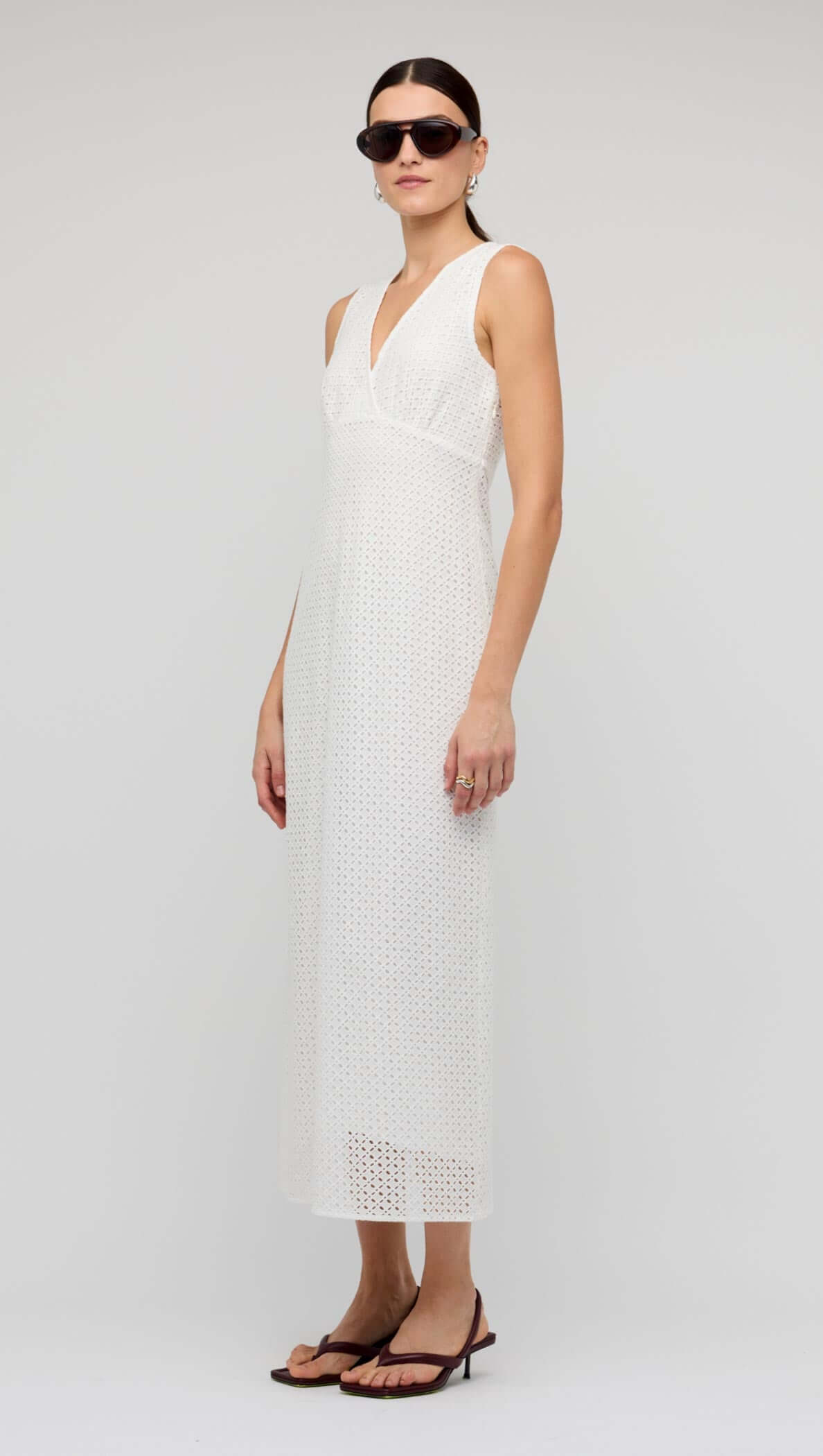 White Broderie Bias Midi Dress worn by a model, showcasing sleeveless V-neck design and delicate broderie detailing.