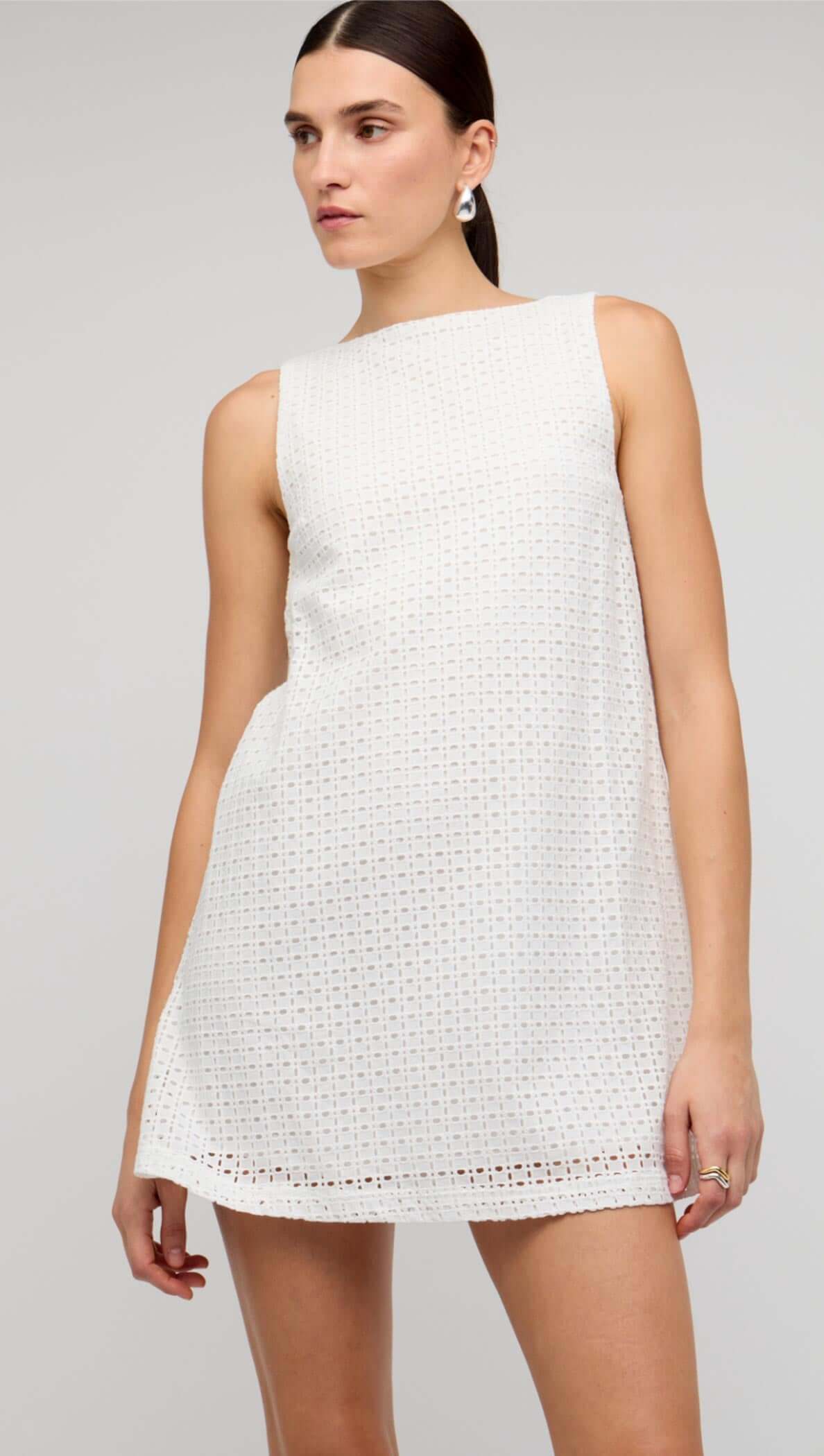 Model wearing a White Broderie Mini Shift Dress by Staple the Label, featuring a sleeveless design and deep V-back.