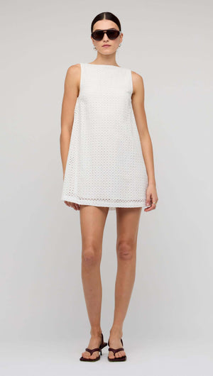 Woman wearing a White Broderie Mini Shift Dress with sunglasses, showcasing a shift silhouette and deep V-back.