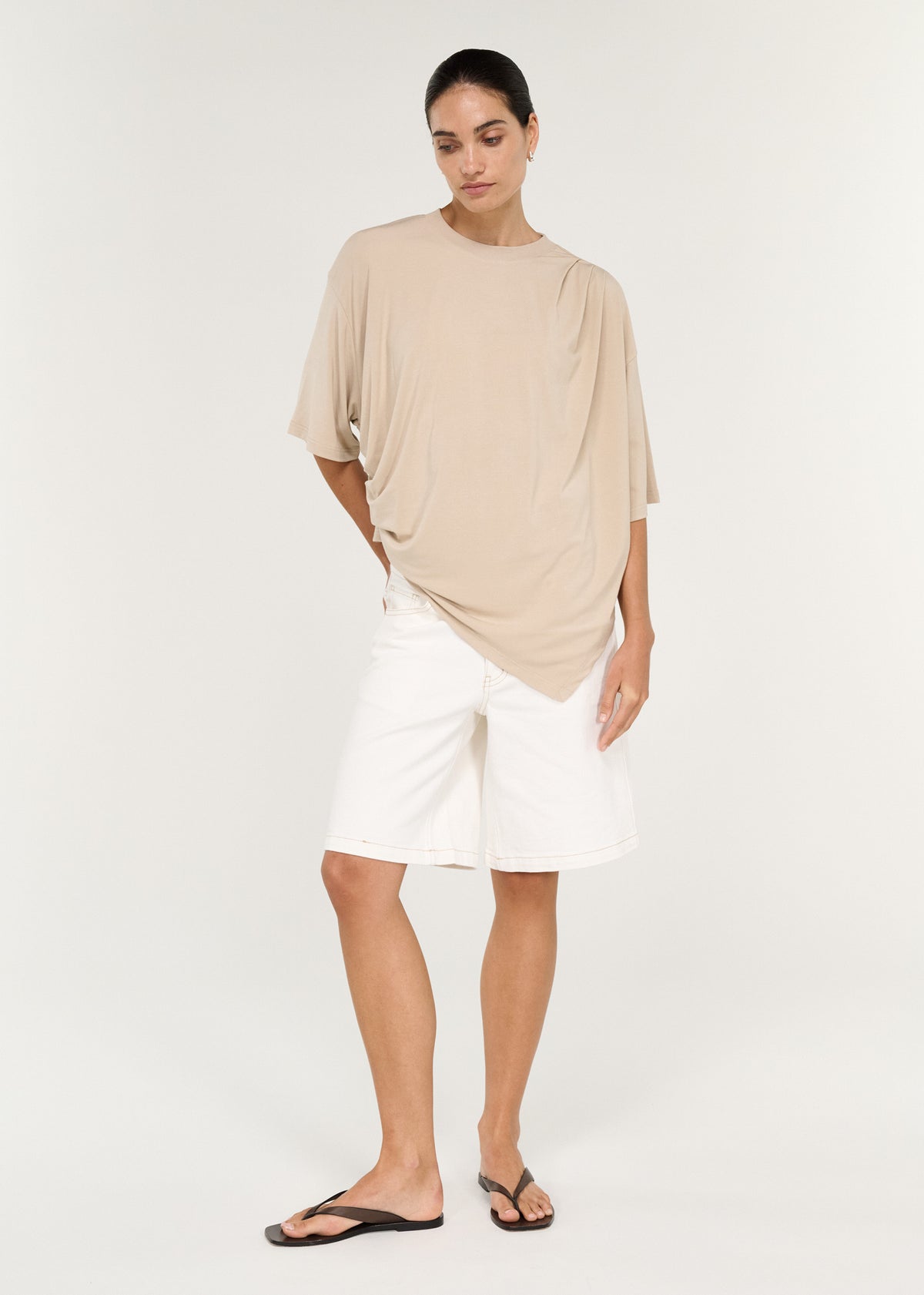 Model wearing Asymmetric Draped Oversize Tee in Beige, showing an asymmetric draped detailing and a crew neckline.