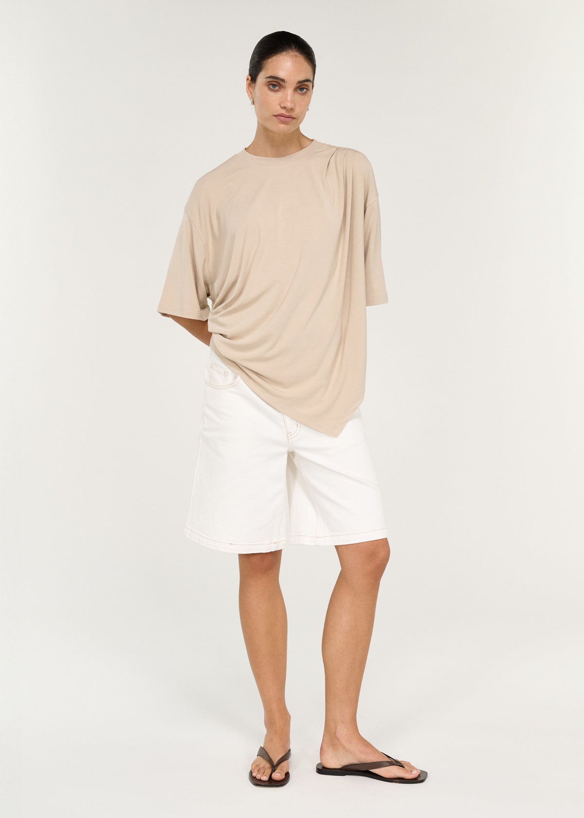 Model wearing Asymmetric Draped Oversize Tee in Beige with an asymmetric hemline and a soft, fluid finish.