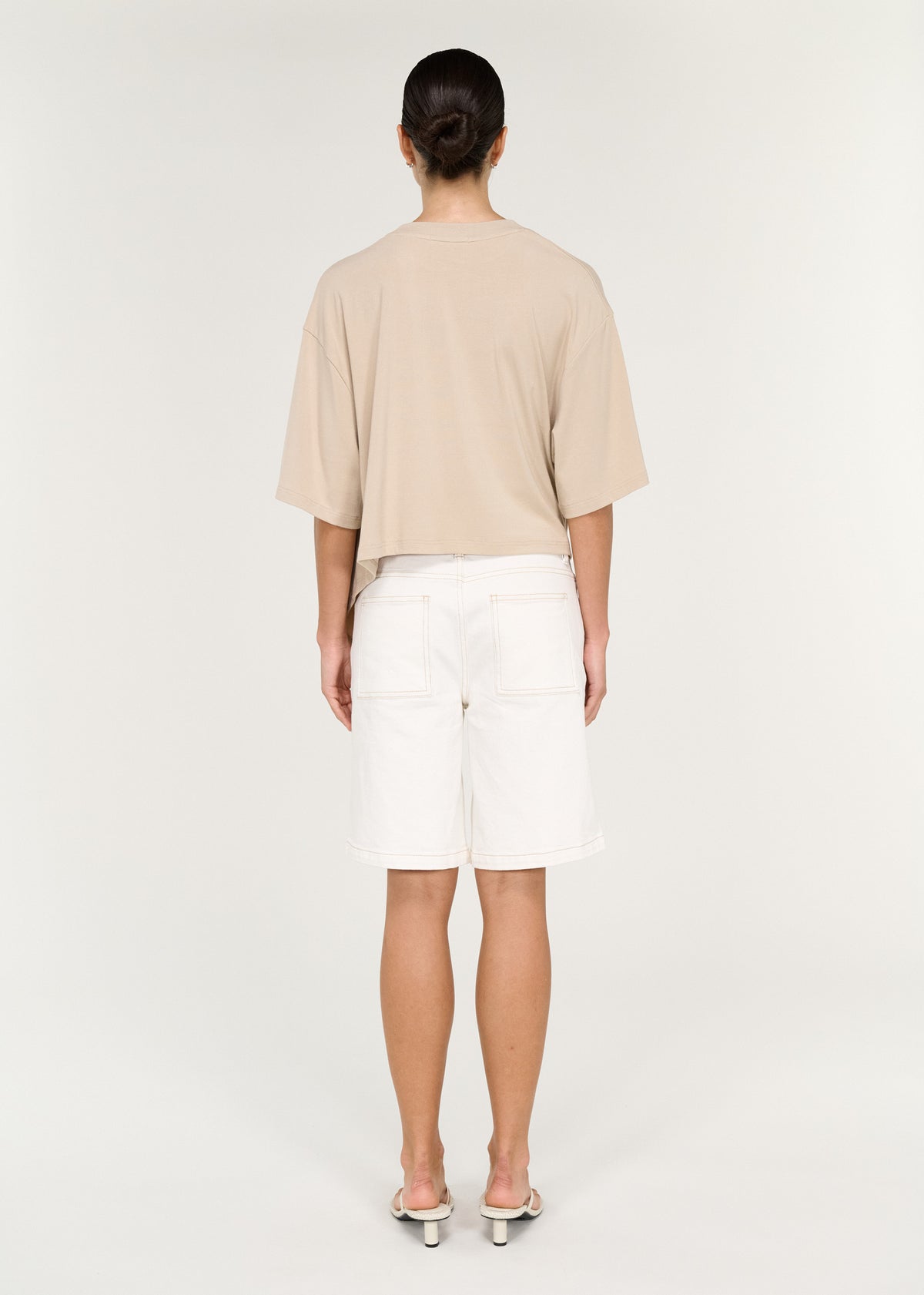 Back view of the Asymmetric Draped Oversize Tee in Beige with a soft fluid jersey fabrication and an oversized silhouette.