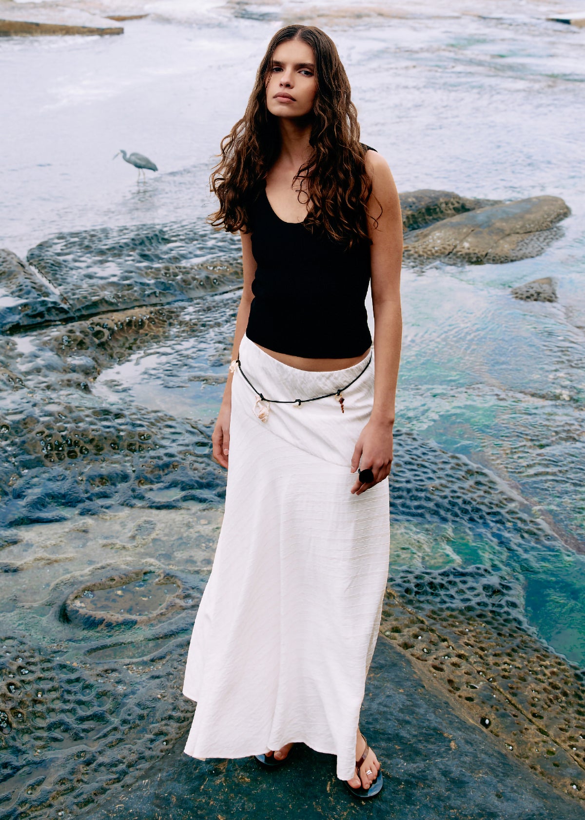 Model wearing Asymmetric White Bias Maxi Skirt with a maxi length and a lightweight, breathable fabric, turned to the side.