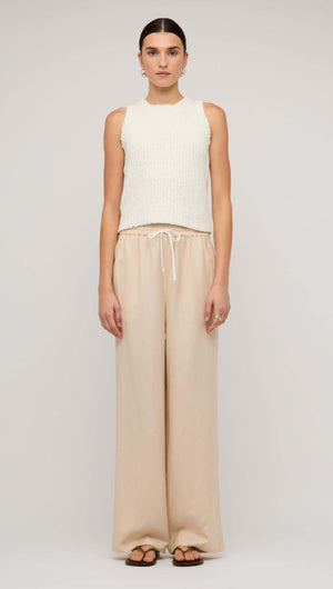 Woman wearing beige relaxed linen wide-leg pants paired with a cream knitted tank top.