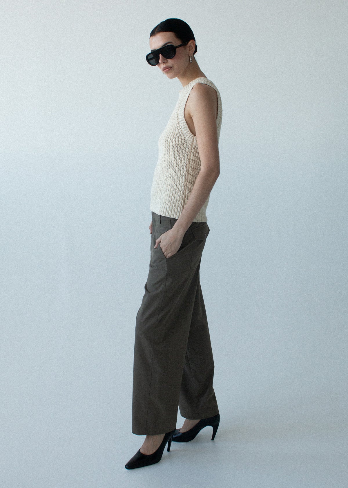 Model wearing Beige Sleeveless Knit Tank Top with a ribbed hem and neckline detailing, turned to the side.