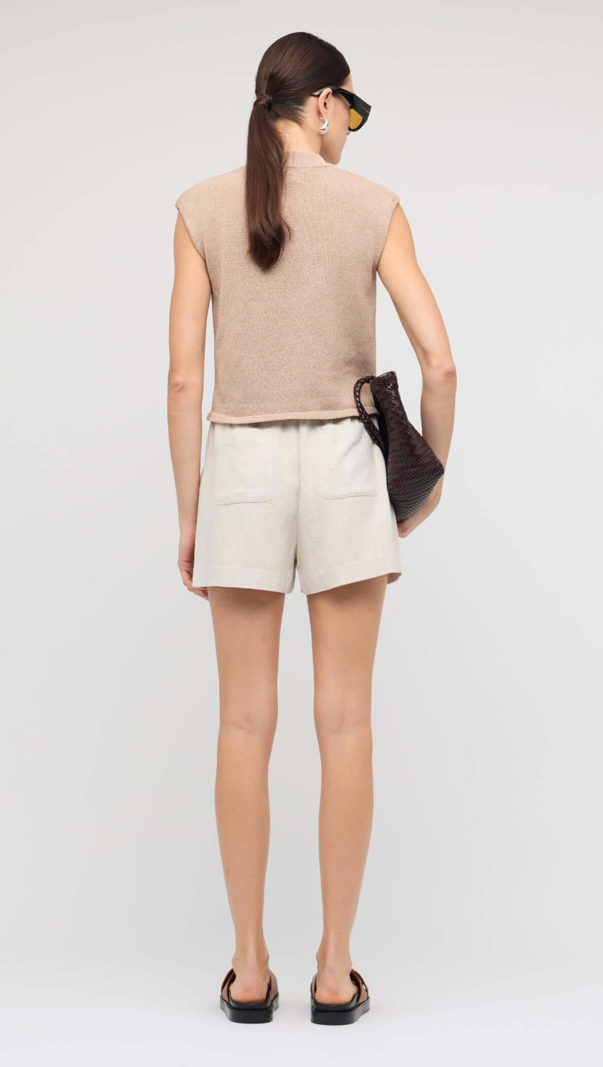 Back view of a model wearing a Beige Sleeveless Knit Top paired with linen shorts.
