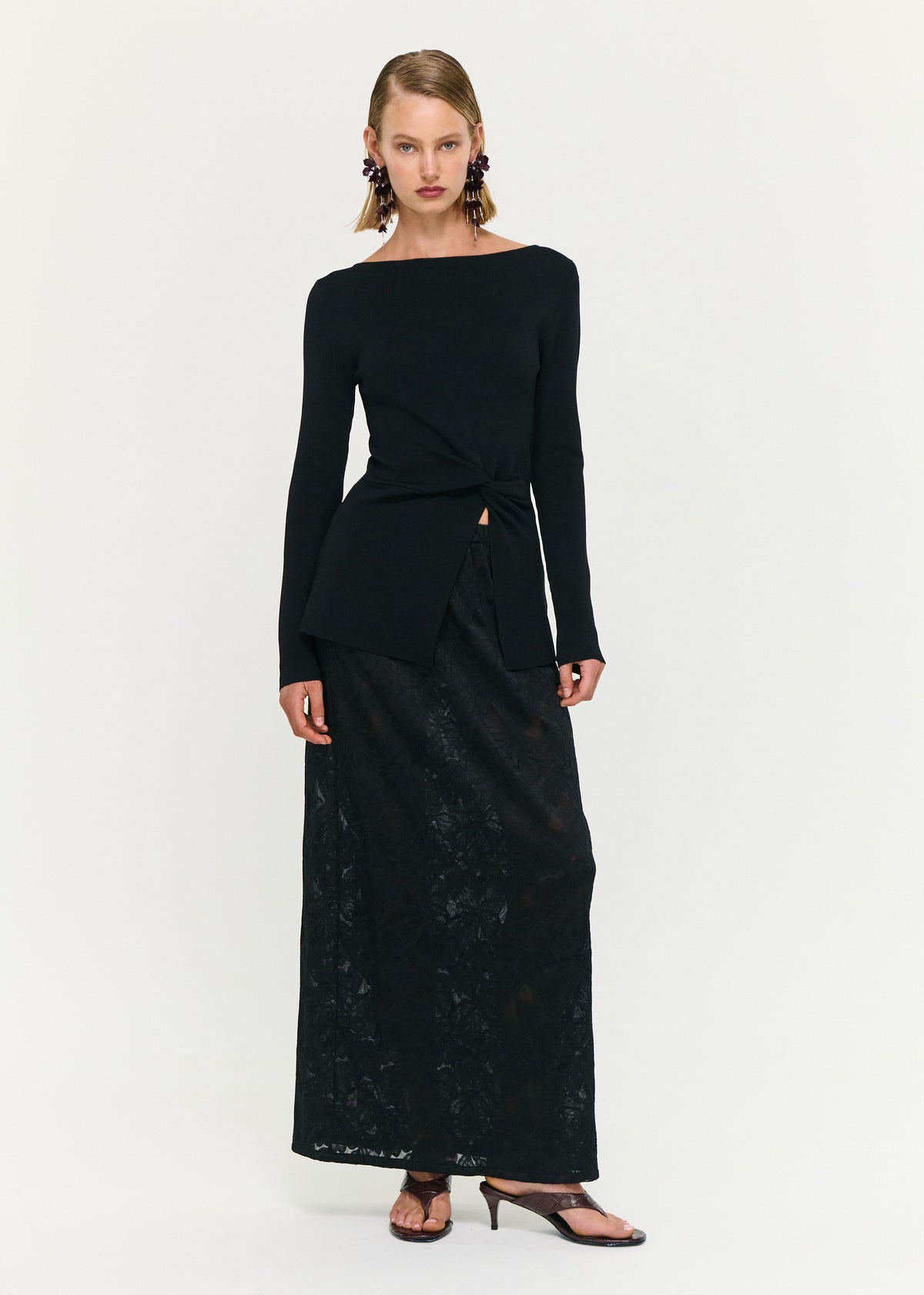 Model wearing Black Boat Neck Twist Knit Top, showing a twist detail at waist and an asymmetric hem finish.