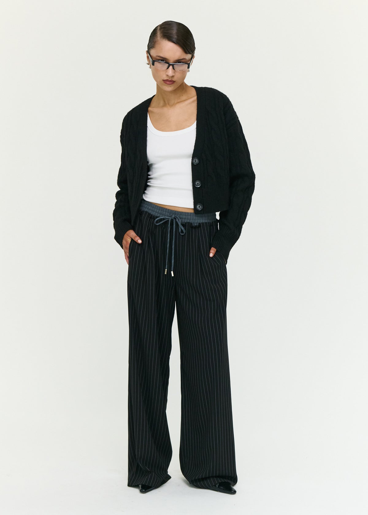 Model wearing Black Cable Knit Cropped Cardigan with a cropped length and long sleeves, turned to the side.