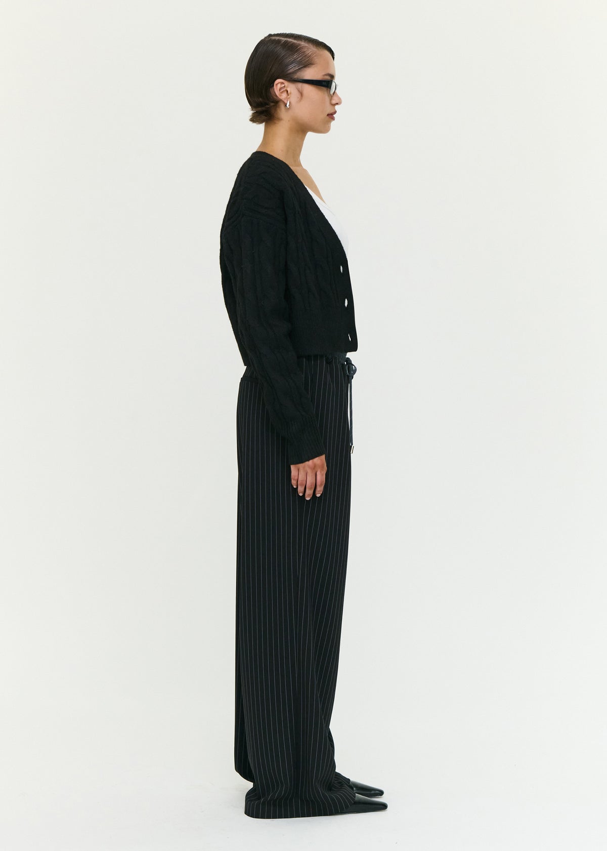 Side view of the Black Cable Knit Cropped Cardigan, showing a soft cable knit fabrication and a relaxed fit.